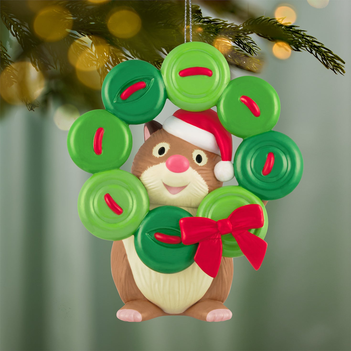 Cute as a Button, 4th in the Series — 2026 Hallmark Keepsake Christmas Ornament featuring a happy hamster wearing a Santa hat and holding a button wreath, close up.