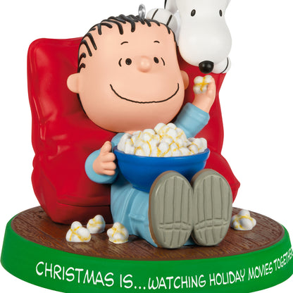 The Peanuts® Gang Christmas Is...Watching Holiday Movies Together, 3rd in the Series — 2026 Hallmark Keepsake Christmas Ornament, featuring Linus and Snoopy sharing popcorn in a red chair.