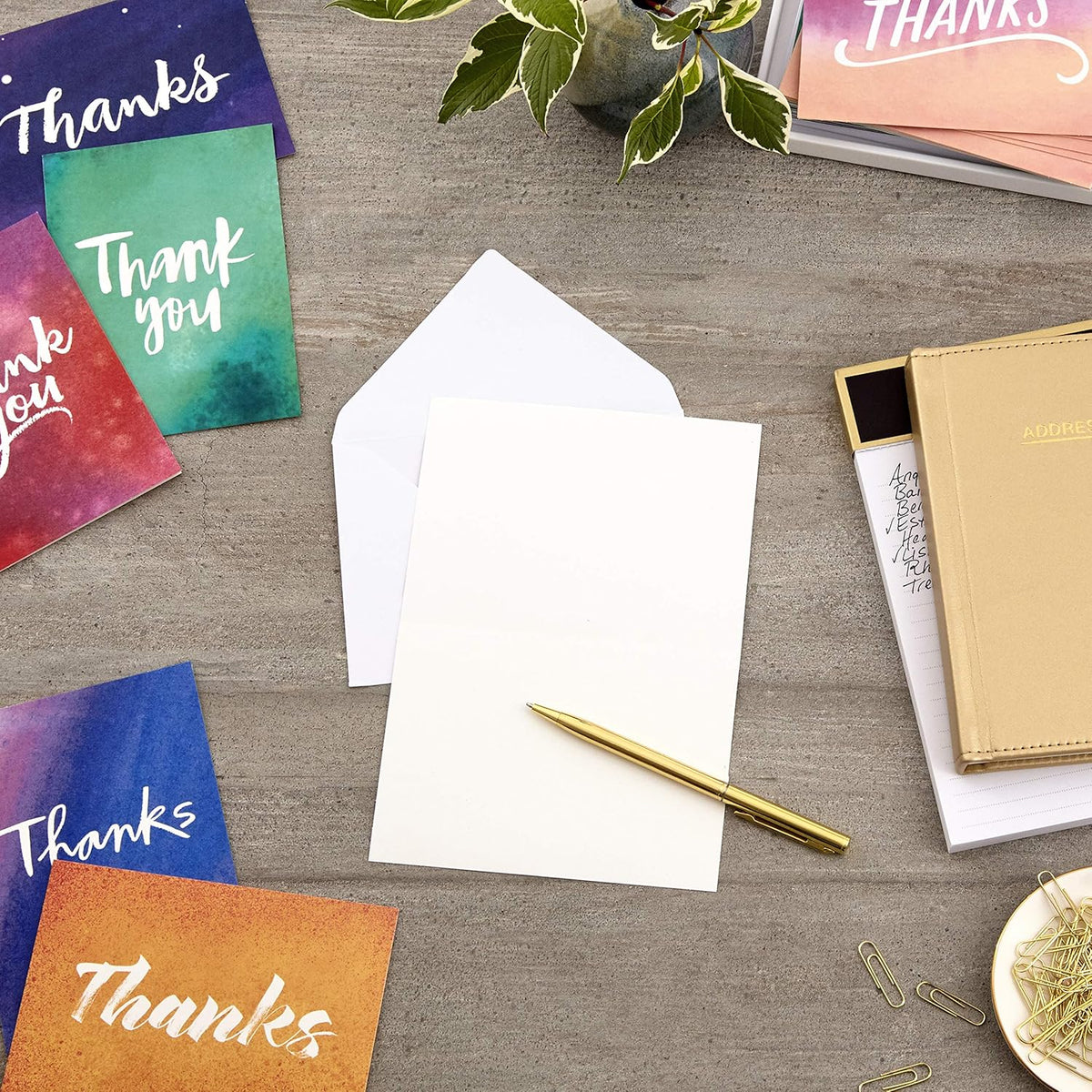Hallmark Thank You Cards Assortment, Watercolor Thanks displayed on a wooden table, featuring colorful cards, envelopes, and a gold pen.
