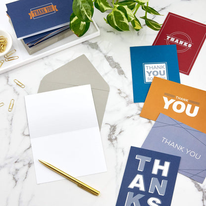 Hallmark Thank You Cards Assortment, Bold Type featuring six colourful designs on a marble surface with a gold pen and envelopes.