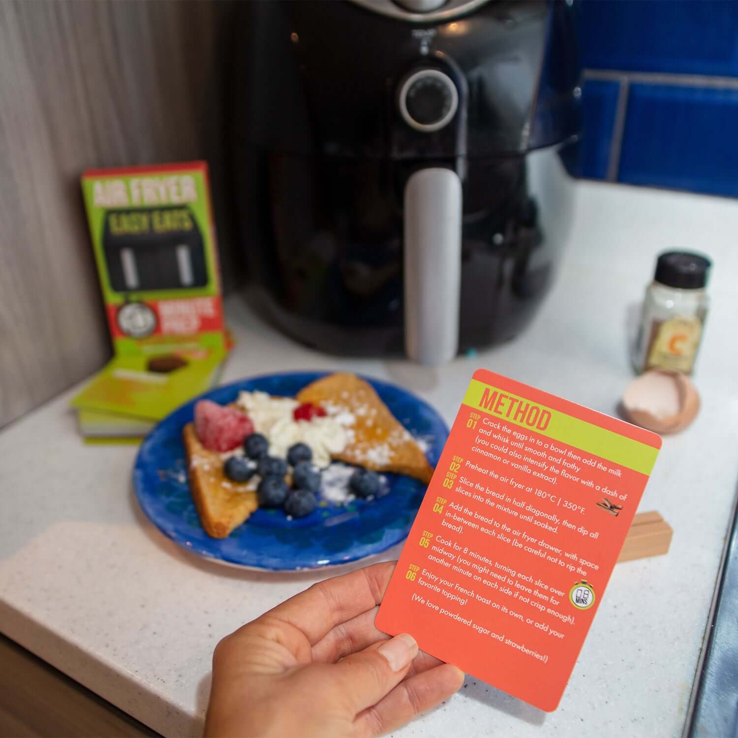Easy Eats Air Fryer Recipe Cards displayed next to a plate of air-fried pastry with berries, in a kitchen setting.