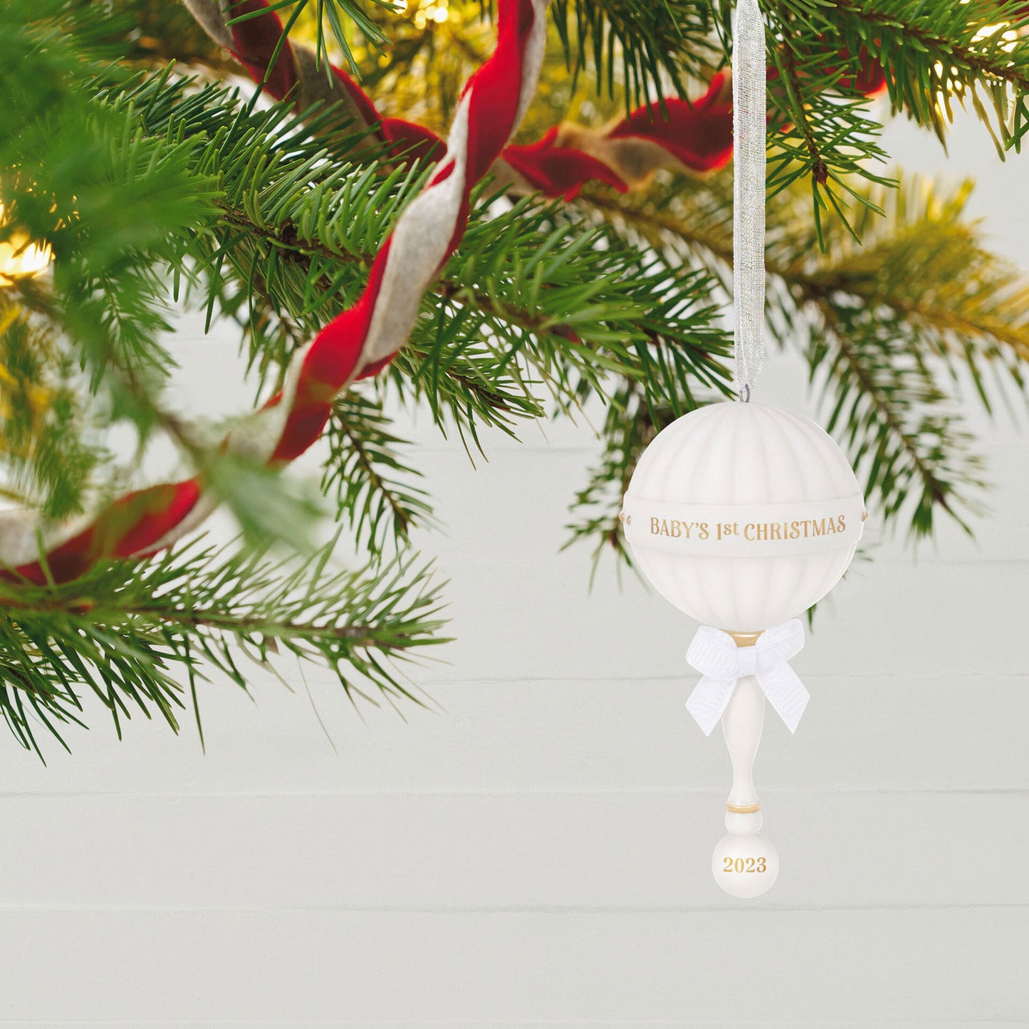 Baby's First Christmas (2023) Porcelain Rattle — Hallmark Keepsake Christmas Ornament hanging on a Christmas tree with gold accents and white bow.