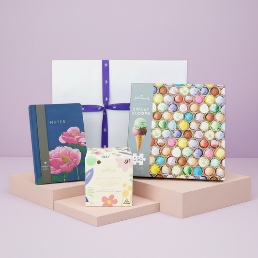 Collection of stationery items including notebooks and a gift box on a light pink platform with a light purple background.