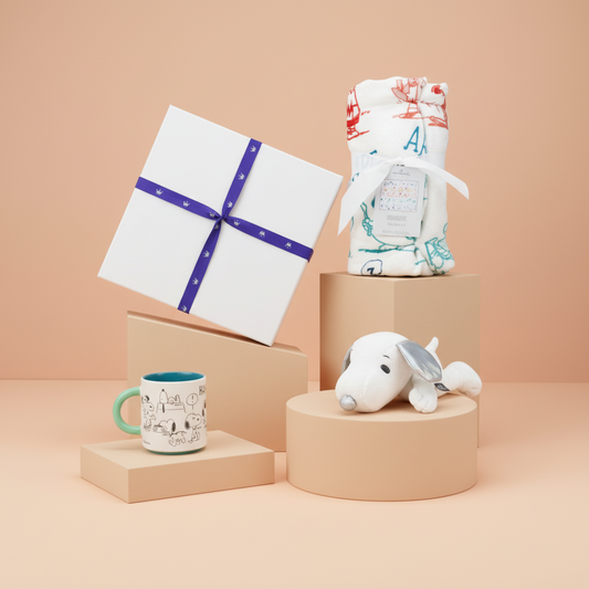 Peanuts Snoppy Gifts including a mug, wrapped item, and plush toy on beige platforms against a beige background