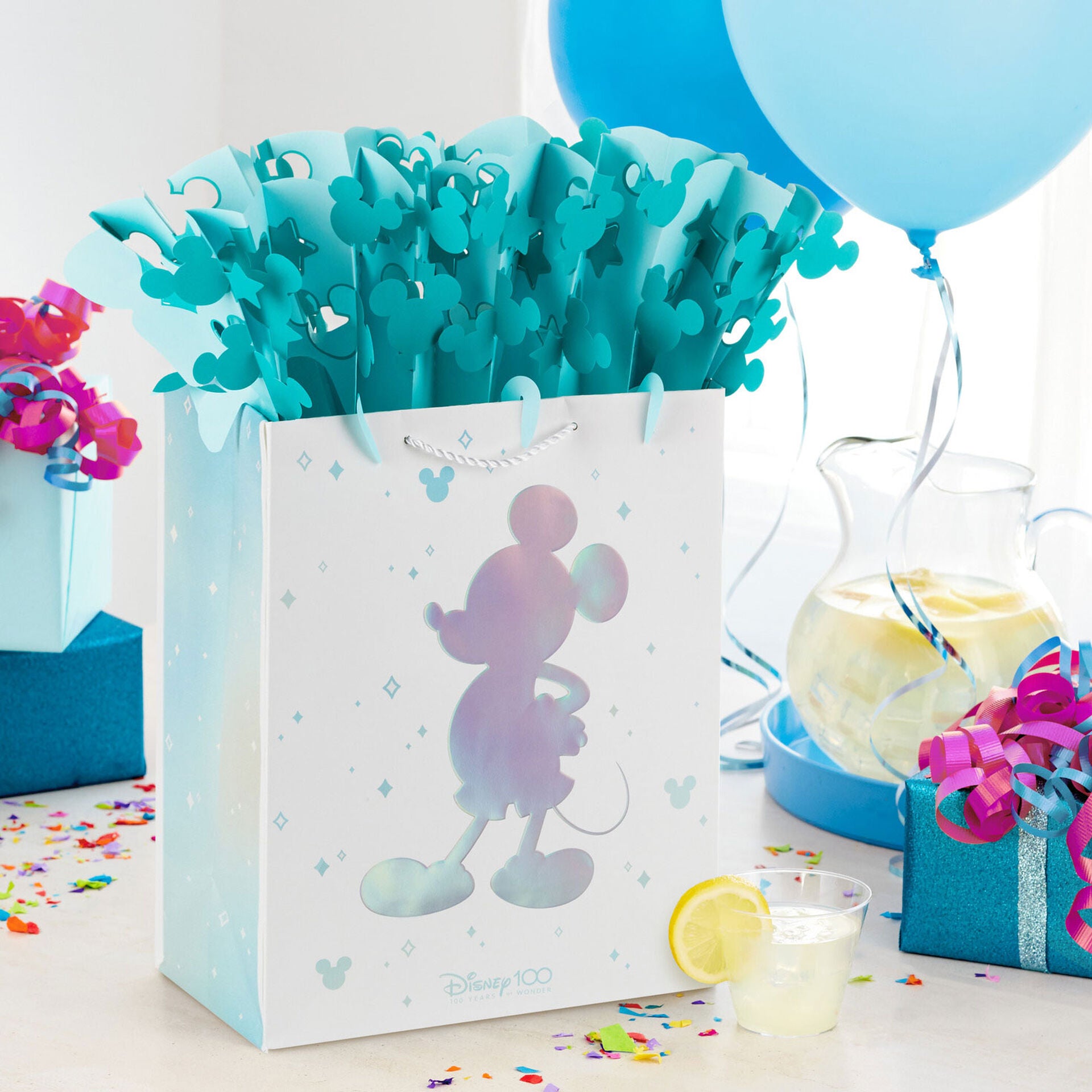 Disney 100 Years of Wonder large gift bag with WonderFill topper, featuring blue Mickey Mouse silhouette and paper, festive setting.