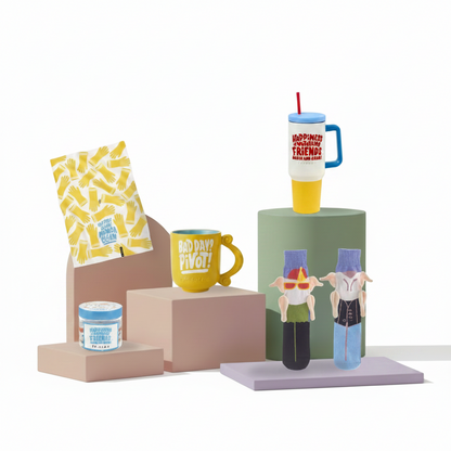 A collection of colorful merchandise displayed on minimalist geometric pedestals against a white background, including a yellow mug that reads 'NO DAY WITHOUT PIVOT!', a patterned snack bag, a small jar, a tall handled tumbler with a cartoon character, and two small character figurines.
