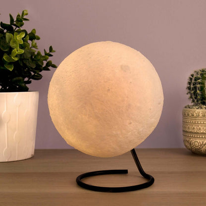 Gift Republic - Moon Lamp in a stylish stand, softly glowing against a purple backdrop, with decorative plants in the background.