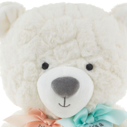 Gender reveal teddy bear plush with ribbons, white plush material, close-up of bear's face showing pink and blue heart charms