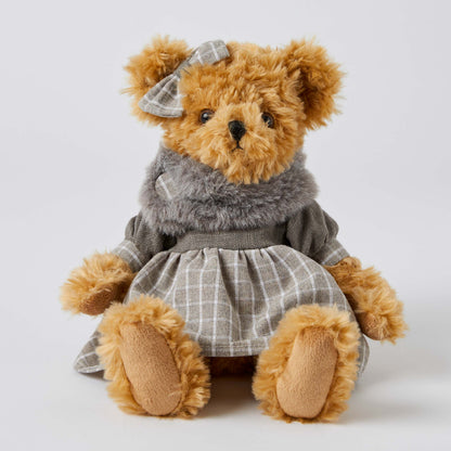 Beatrice the Notting Hill Bear in a grey plaid dress and faux fur scarf, sitting with a bow on her head.