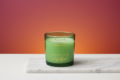 Hallmark Essential Oil Australian Soy Wax Candle - Kakadu Plum & Wildflower in a green glass jar on a marble surface with a gradient background.