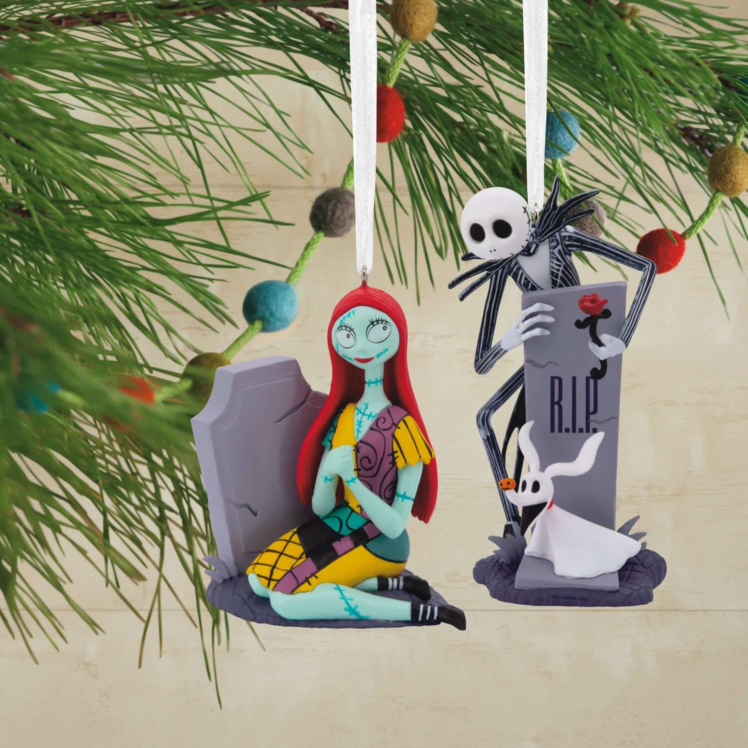 Disney Tim Burton's The Nightmare Before Christmas Jack and Sally with tombstones, set of 2 ornaments, hanging among greenery with a festive background.