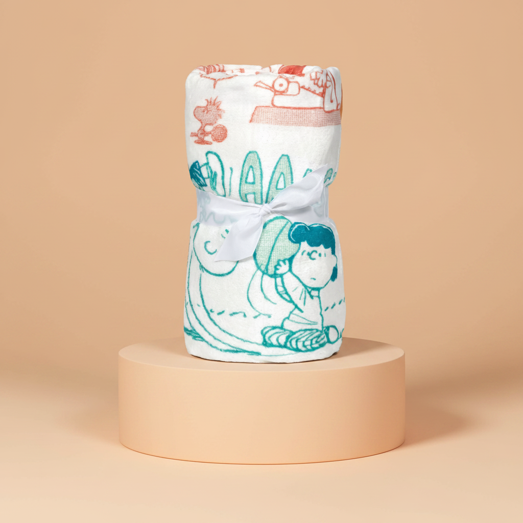 Peanuts Snoppy Swaddle blanket with cartoon characters on a beige platform and background