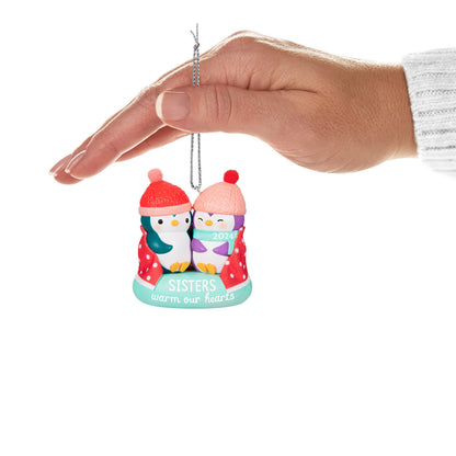 Sisters Warm Our Hearts — Hallmark Keepsake Christmas Ornament featuring two penguins in hats, held in hand with a festive colour scheme.