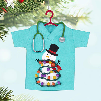 The Caring Spirit, Nurses — 2025 Hallmark Keepsake Christmas Ornament in teal scrubs shirt with snowman and lights, close-up view.