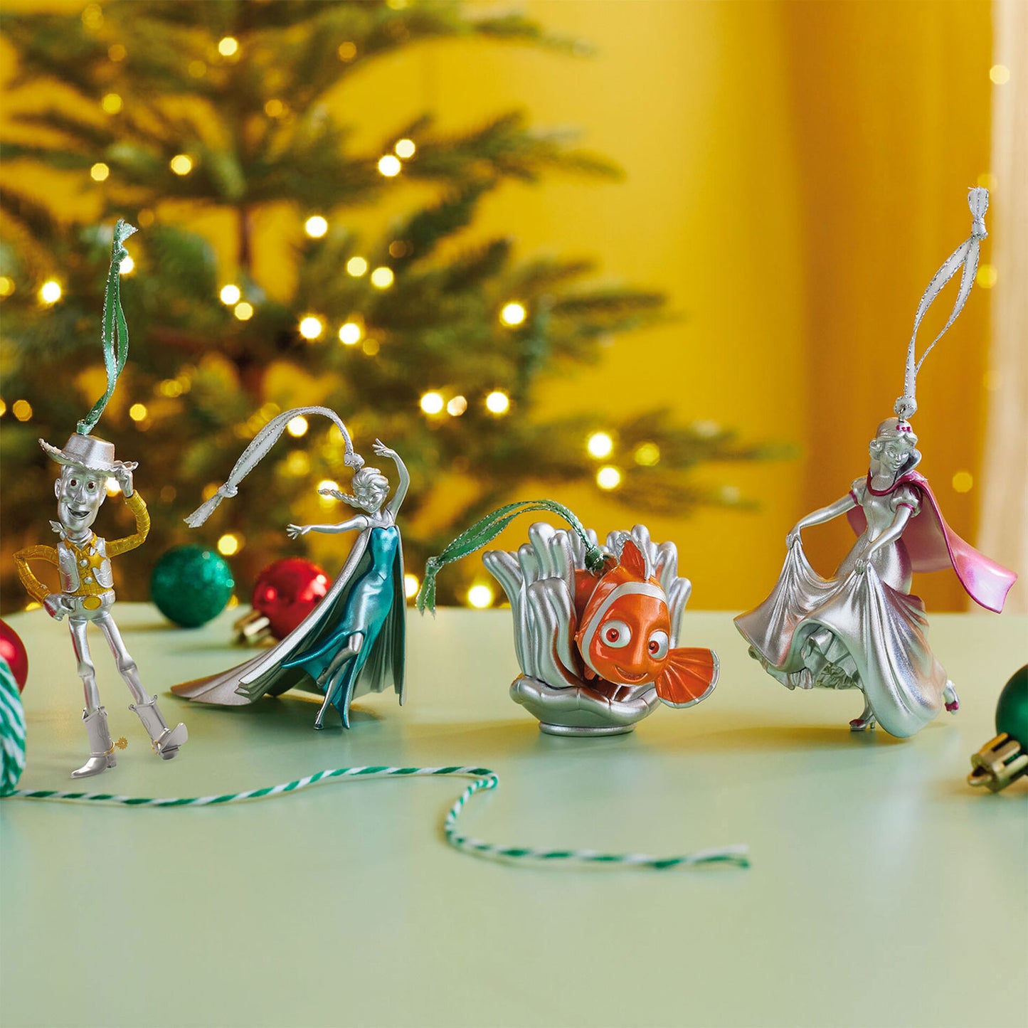 Disney 100 years of wonder Pixar and princesses, set of 4 — Hallmark keepsake Christmas ornament displayed on a green table with a Christmas tree.