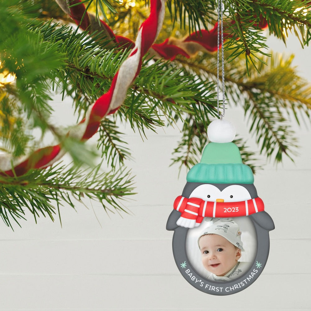 Baby's 1st Christmas (2023) photo frame — Hallmark Keepsake Christmas ornament featuring a penguin with a scarf and baby photo holder, hung on a tree.