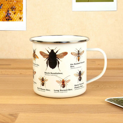 Gift Republic - Bee Enamel Mug with various bee illustrations on a white enamel surface, set against a wooden table.