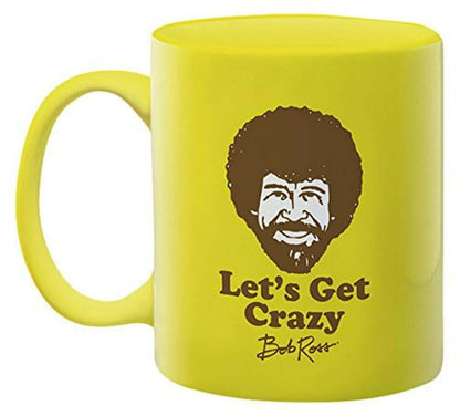 Bob Ross - Let's Get Crazy Ceramic Mug in bright yellow with a smiling face design and black text, angled view showcasing handle.