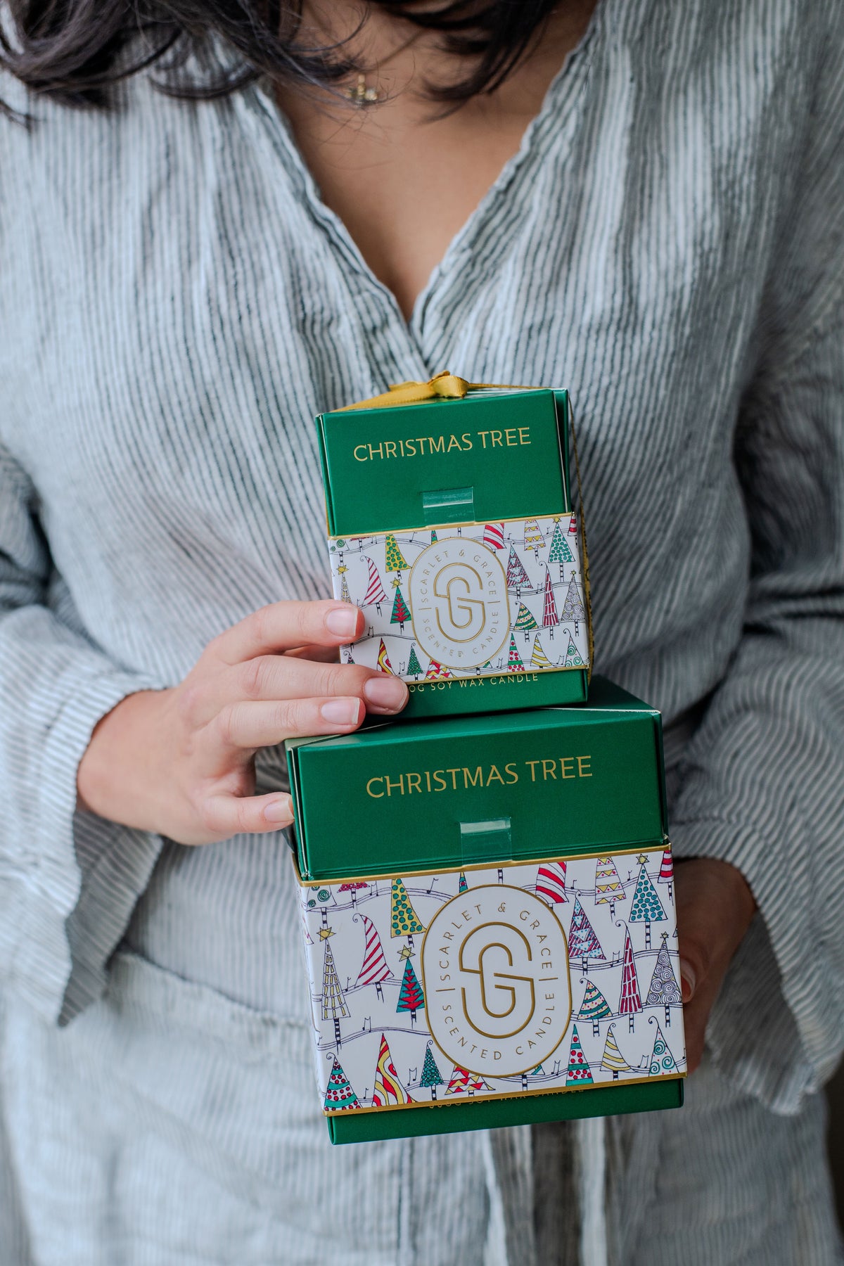 Christmas Tree Candle - Limited Edition (380g) stacked gift boxes held by a person, featuring festive tree designs and green packaging.