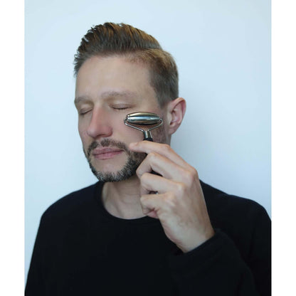 5 cooling facial roller being used by a man, silver stainless steel tool, close-up view, facial massage