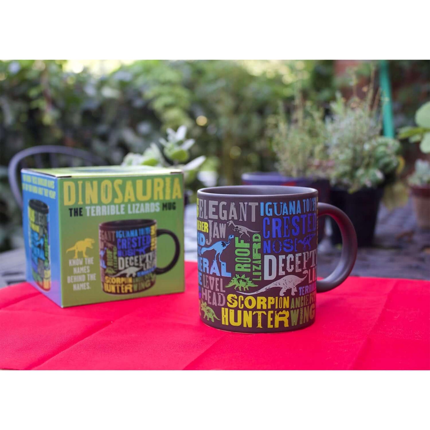 Unemployed Philosophers Guild - Dinosaur Mug featuring colourful dinosaur-themed designs with packaging on a red table.