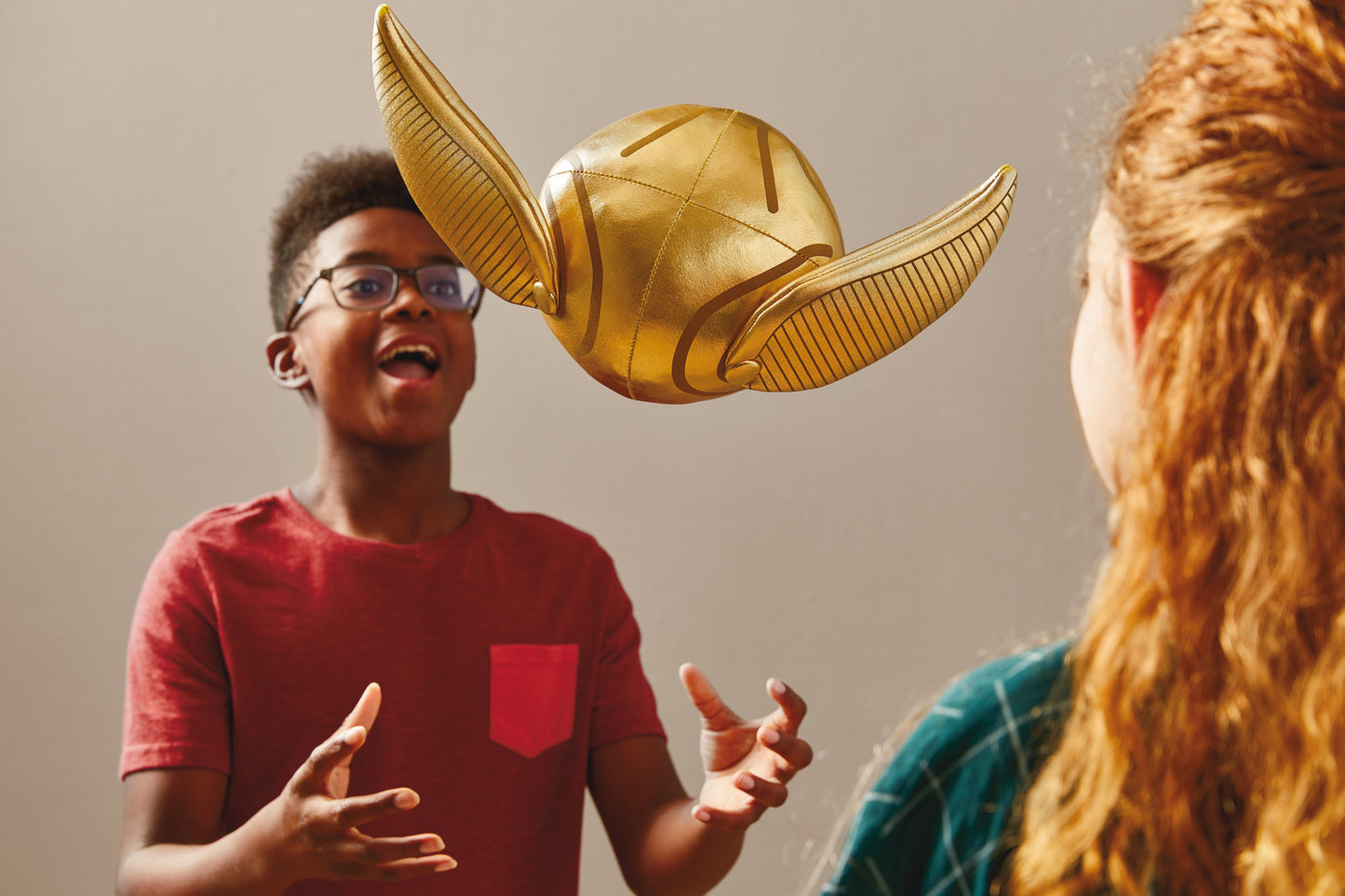 Harry Potter™ Golden Snitch™ Musical Plush With Motion, 8" being tossed by a young boy in a red shirt with a friend watching.