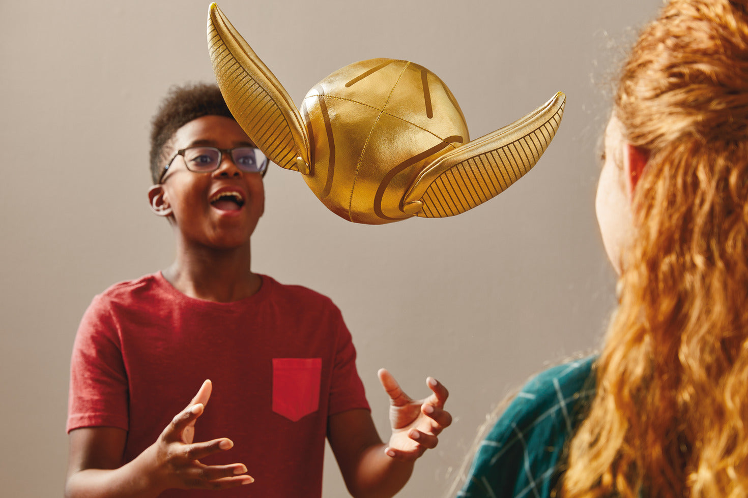 Harry Potter™ Golden Snitch™ Musical Plush With Motion, 8" being tossed by a young boy in a red shirt with a friend watching.