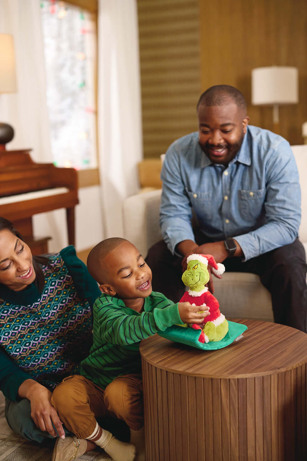 Dr. Seuss's How the Grinch Stole Christmas!™ Grinch on Sled Musical Plush With Motion sitting on a table, child excitedly pressing its hand.