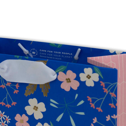 Hallmark Medium Gift Bag - Sky Blue Floral with white ribbon handles and floral design detail, angled view showing care instructions.