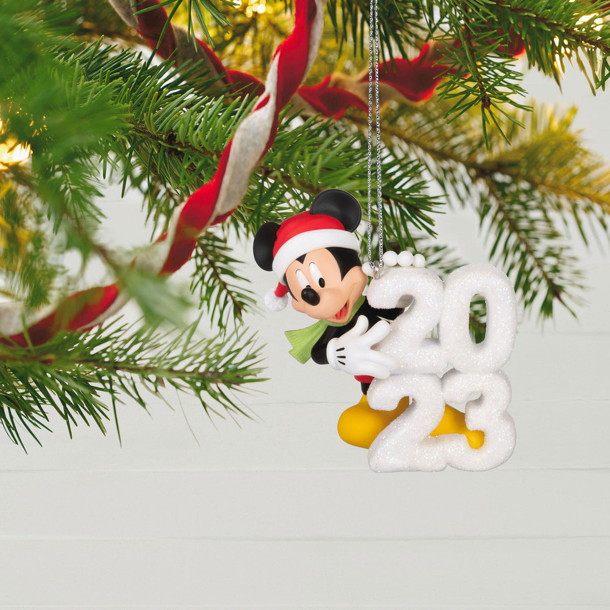 Disney Mickey Mouse, A Year of Disney Magic — Hallmark Keepsake Christmas Ornament hanging from a Christmas tree, featuring a Santa hat and '2023' snow sculpture.