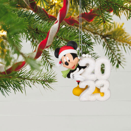 Disney Mickey Mouse, A Year of Disney Magic — Hallmark Keepsake Christmas Ornament hanging from a Christmas tree, featuring a Santa hat and '2023' snow sculpture.