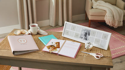 My First Year Baby Book - Blue on a coffee table with a cup of tea, gingerbread biscuits, and a photo frame.