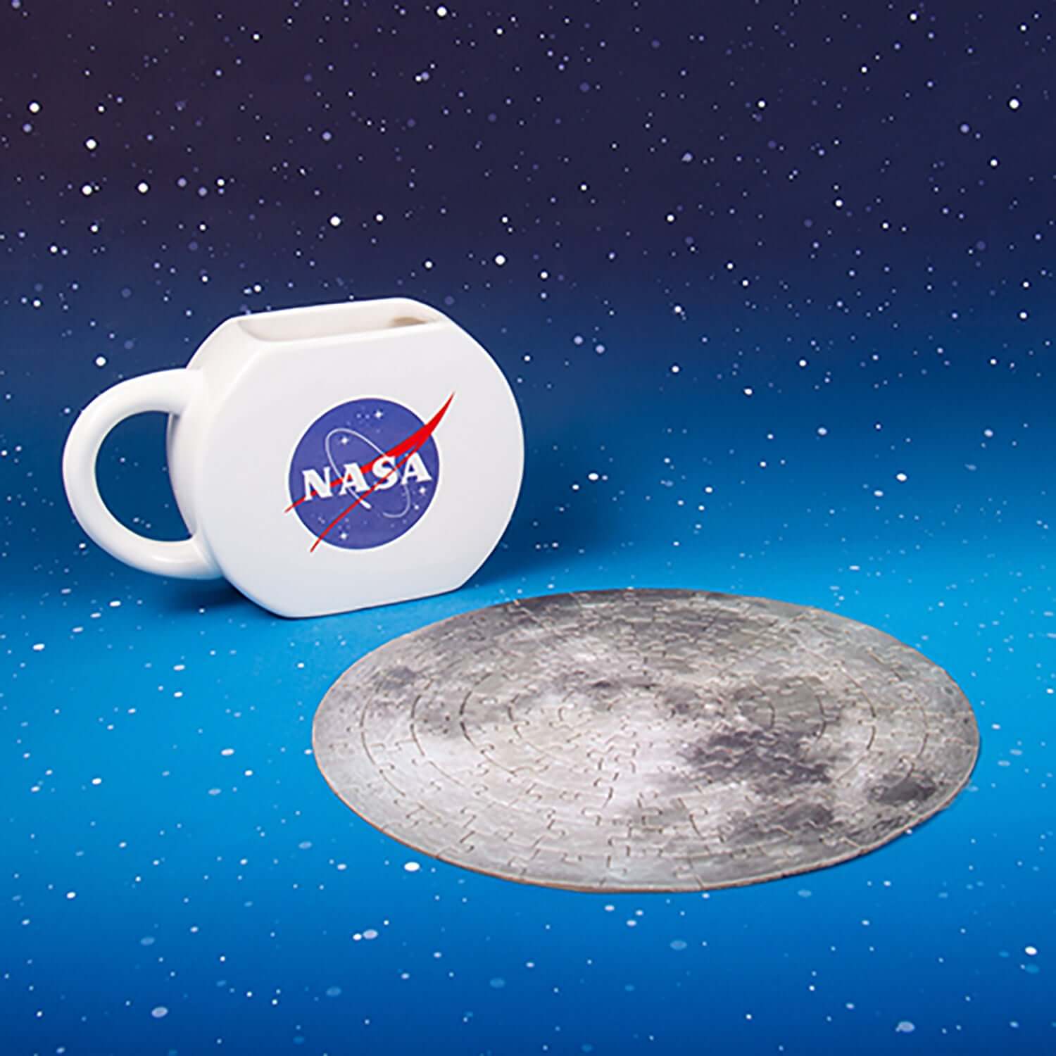 NASA Mug & Puzzle set featuring a circular moon puzzle and a white ceramic mug with the iconic NASA logo, angled view on a starry background.