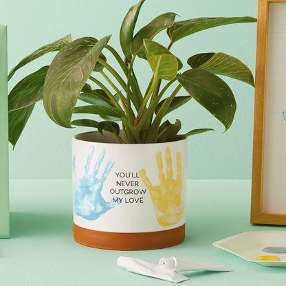 Never Outgrow My Love Planter Handprint Kit with green plant, featuring colourful handprints and a ceramic design, flat lay view.