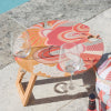Abstract foldable picnic table in vibrant colours with wine glass beside it, positioned near a poolside.