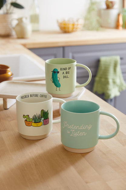 Pretending to Listen Funny Mug, 473ml in aqua blue with a humorous message, positioned alongside two other decorative mugs on a kitchen countertop.