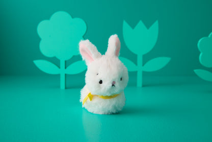 Hallmark Zip-a-Long Bunny Stuffed Animal in white plush, featuring a yellow ribbon, posed with vibrant paper flower cutouts.